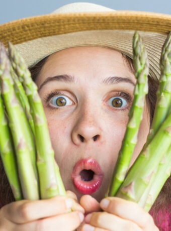 Mujer frustrada sujeta espárragos representando la frustración de ser vegano y comiendo fuera en restaurantes típicos.