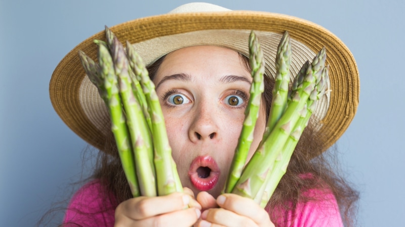 Mujer frustrada sujeta espárragos representando la frustración de ser vegano y comiendo fuera en restaurantes típicos.