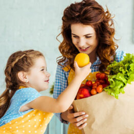 Una mamá y su hija sacar frutas y verduras de la bolsa de compras.