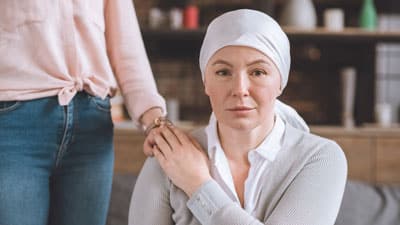 Una mujer sometida a tratamiento contra el cáncer sostiene la mano de otra mujer.