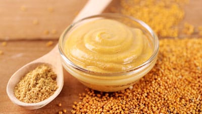 A bowl of mustard next to some other food.
